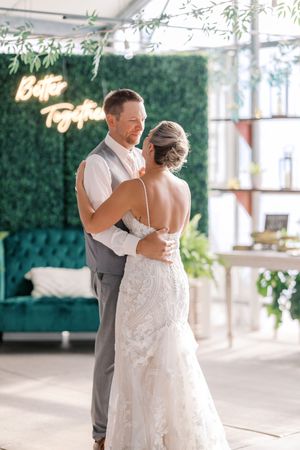 A couple shares an intimate dance moment in a bright indoor venue decorated with hanging greenery.