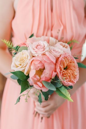 Beautiful peach and blush wedding bouquet with garden roses and ferns held against a coral bridesmaid dress.