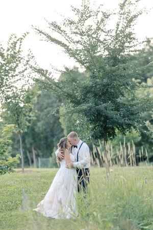 A romantic outdoor wedding photoshoot in a meadow with tall grass and trees in the background.