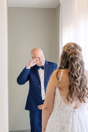 An emotional first look moment between a bride in a lace gown and someone wearing a navy tuxedo with bow tie.