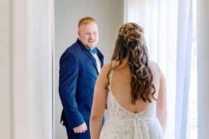 A couple shares a joyful moment during their wedding ceremony in a bright white room with elegant windows.