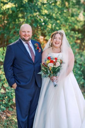 A bride and groom share joyful moments in a garden setting, with the bride wearing a white dress and holding red flowers.