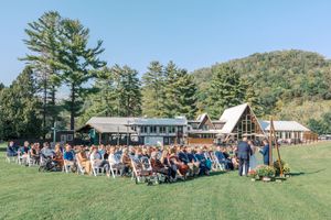 Panoramic view of guests seated in white chairs on a grassy hillside for an outdoor wedding ceremony.