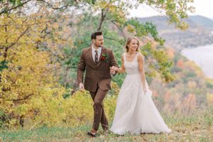 A couple walks arm in arm during an autumn wedding celebration with colorful fall foliage in the mountain backdrop.