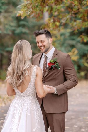 A couple shares a joyful moment outdoors during an autumn wedding, with the bride in white lace and groom in brown suit.