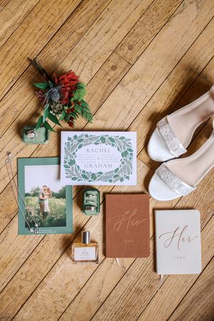 Wedding stationery and invitation suite with floral accents displayed on rustic wooden floor with white shoes.