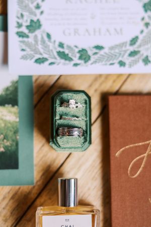 Wedding invitation details and rings arranged artistically on a wooden surface with elegant green and white decor elements.