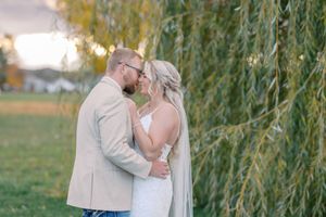 A couple shares a romantic moment under a weeping willow tree during golden hour.