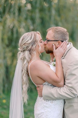 A romantic wedding couple shares a tender kiss in a lush outdoor garden setting with soft bokeh lighting effects.