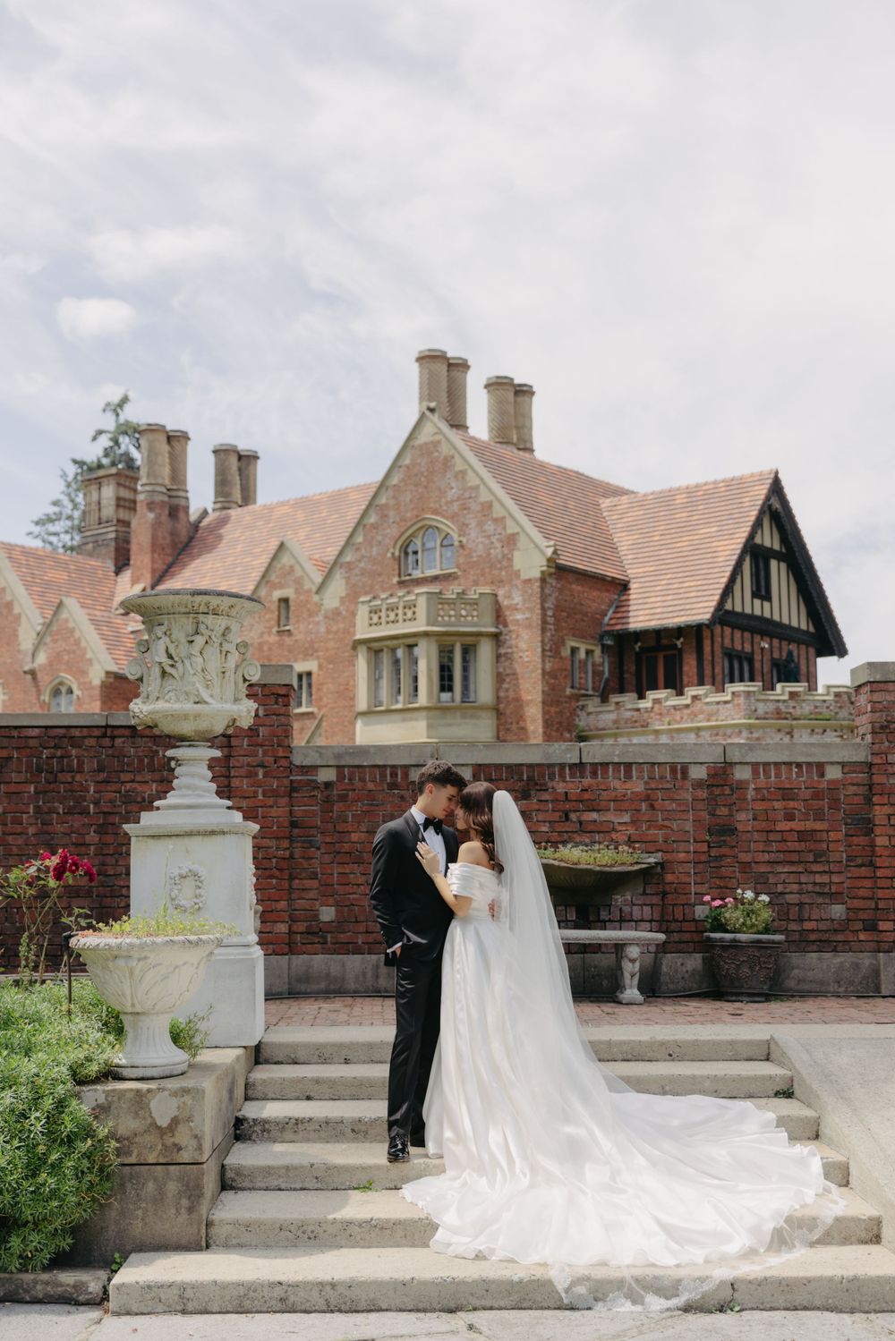 A romantic wedding moment on stone steps in front of a grand brick mansion.