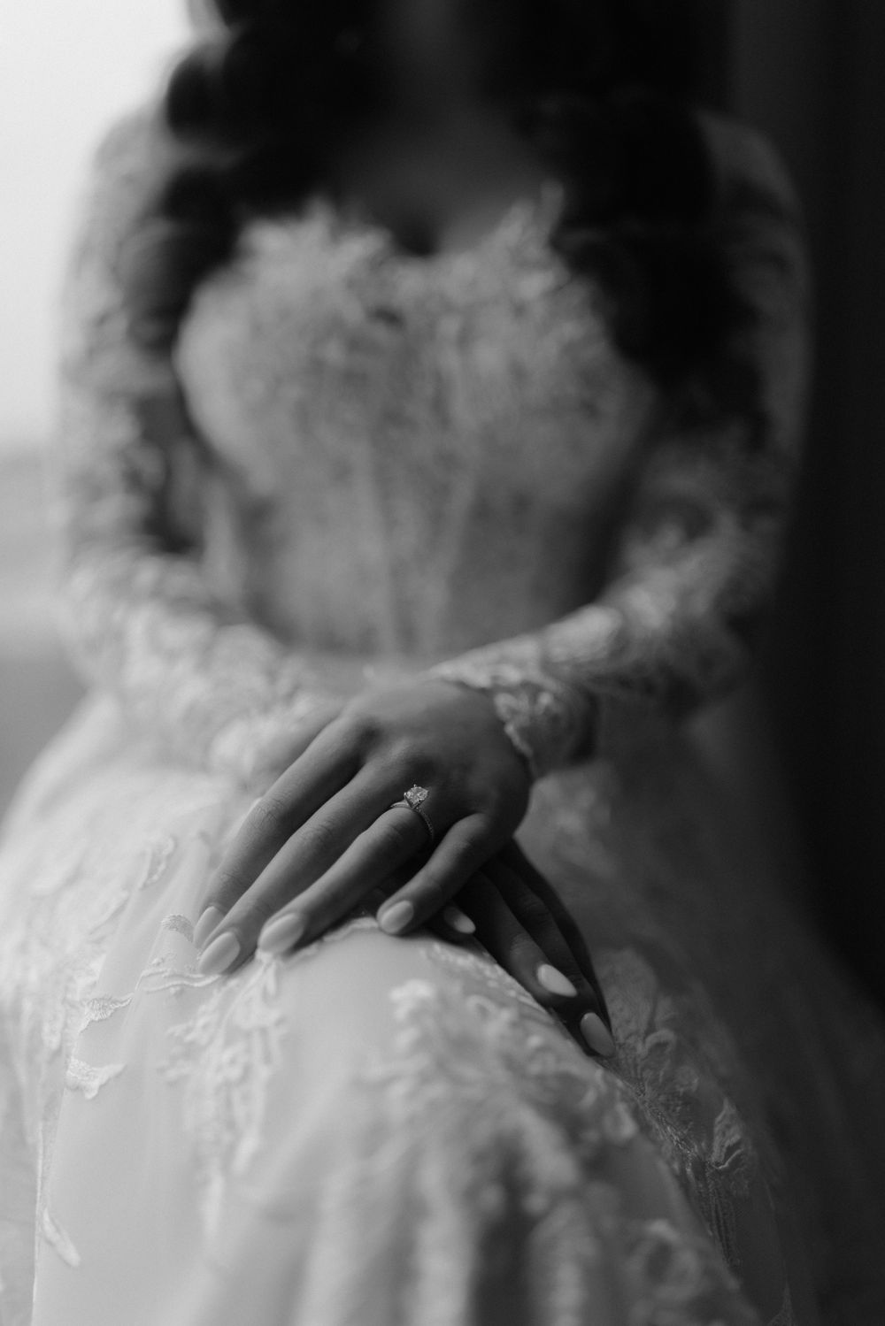 A delicate close-up of a bride's hand resting on her lace wedding dress in black and white.