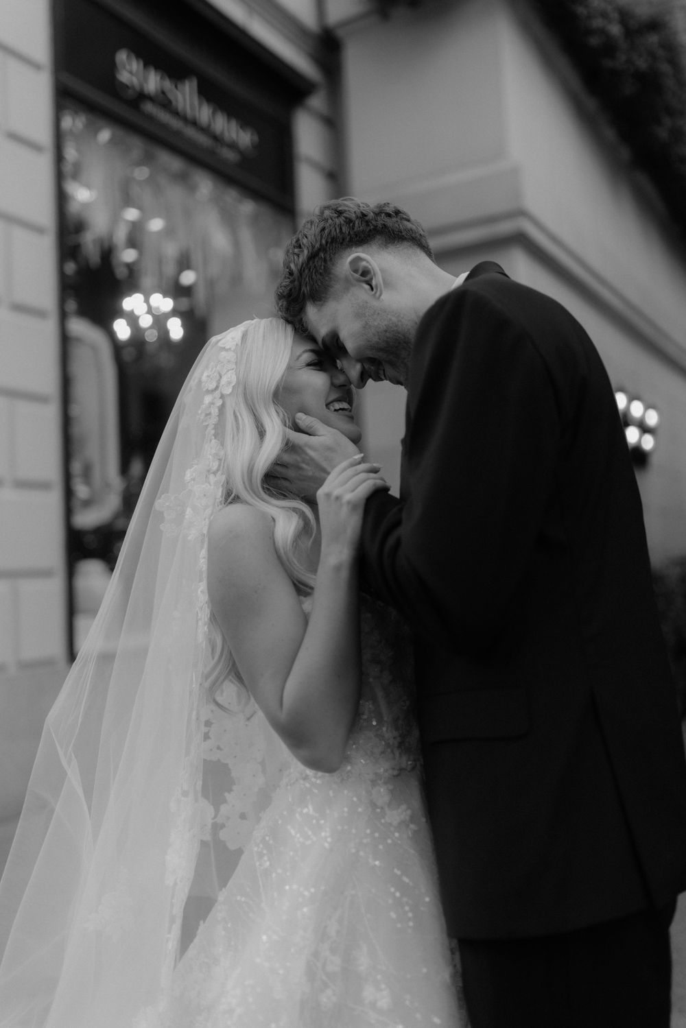 A romantic black and white wedding photo showing a couple sharing an intimate moment outside a store.