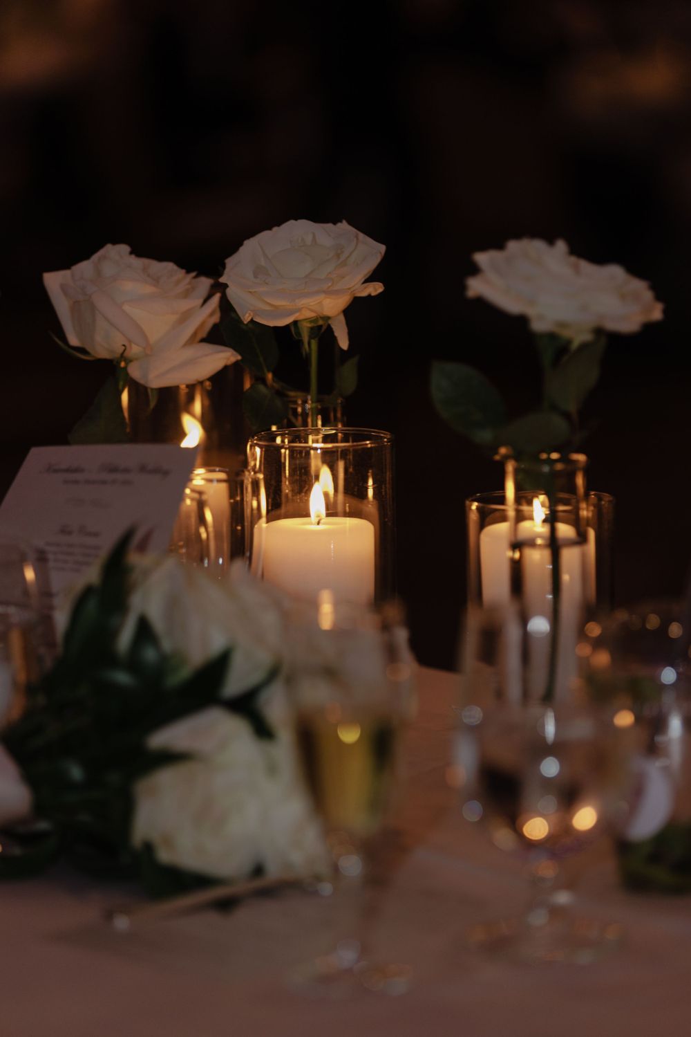 Elegant wedding reception table decor with white roses and glowing candlelight creating a romantic ambiance.