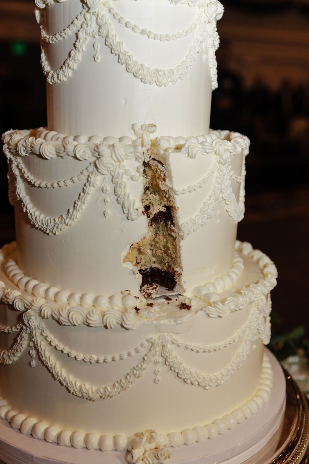 An elegant white tiered wedding cake with piped pearl details and swags displays a cut section revealing chocolate layers inside.