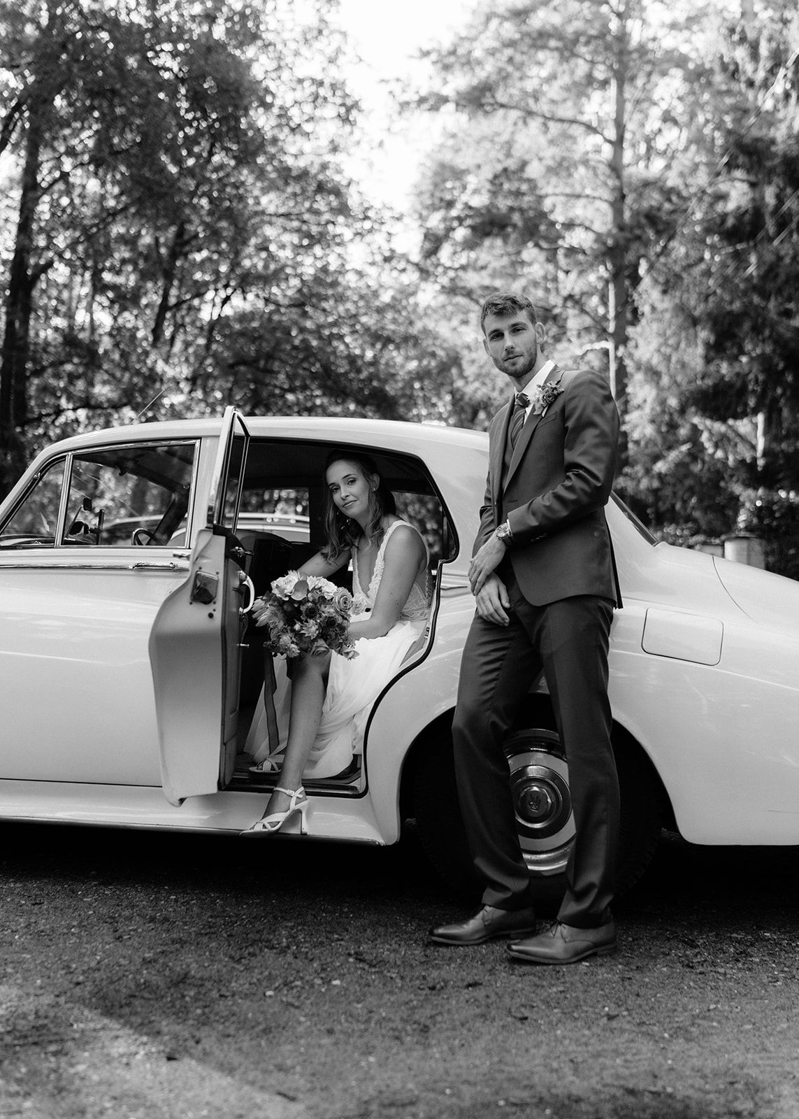 Klassieke vintage auto met bruidspaar in zwart-wit fotografie in editorial stijl.