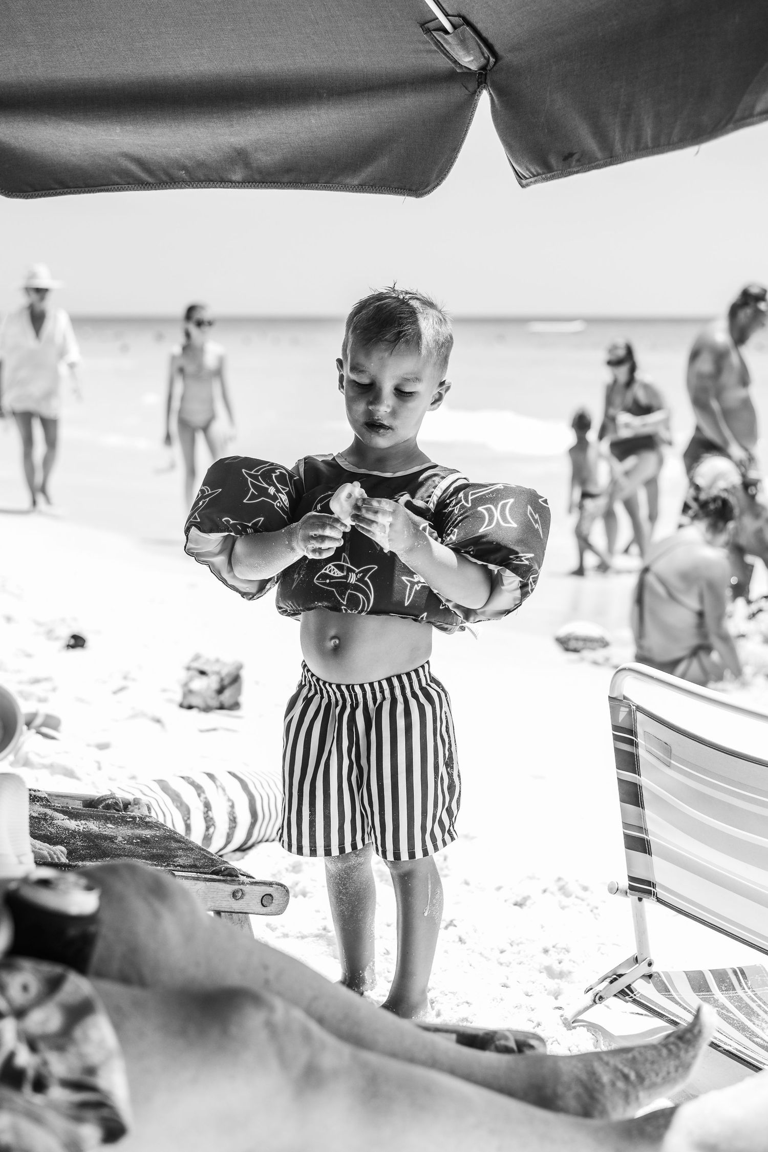 A black and white photo image shows toddlers in vintage-style swimwear playing and exploring at a beach setting.
