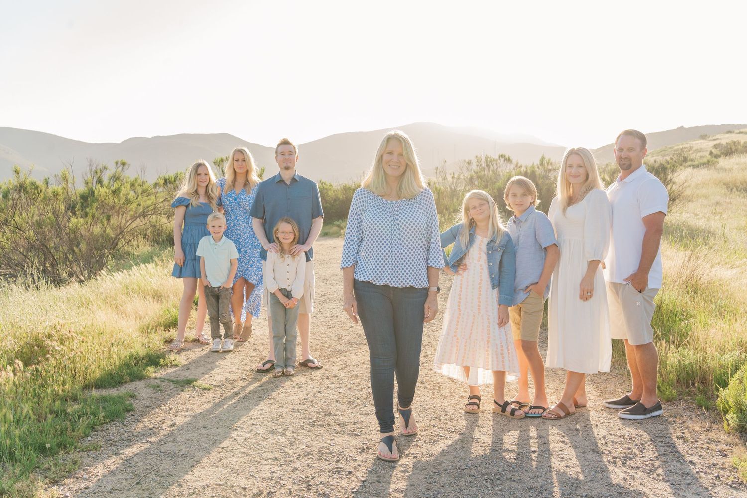 A group in coordinated blue and white outfits walks together on a dirt path during golden hour in a natural setting.