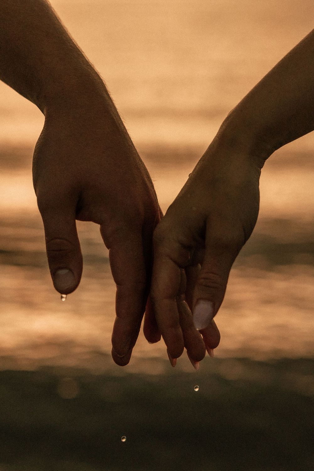 Two hands touching fingertips with water droplets against a golden sunset ocean backdrop.