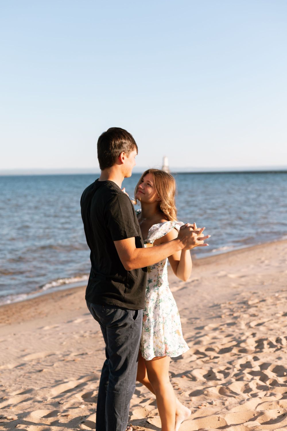 Young couple dancing romantically on a sandy beach at sunset, holding hands near the ocean shoreline.