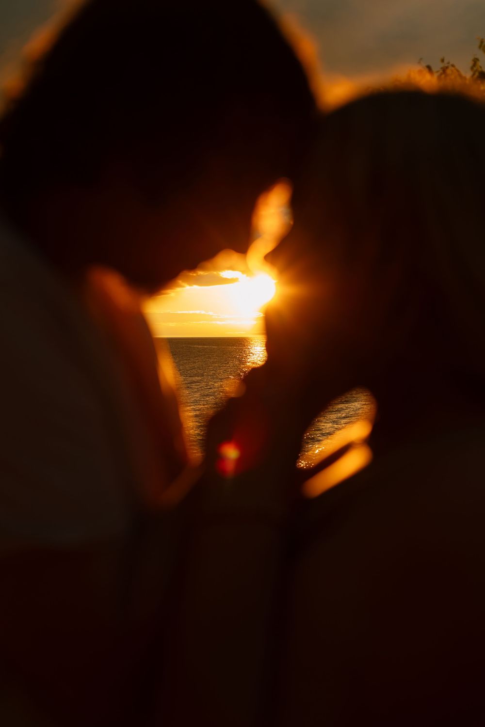 Silhouette of couple almost kissing at golden sunset over ocean, romantic backlit portrait.