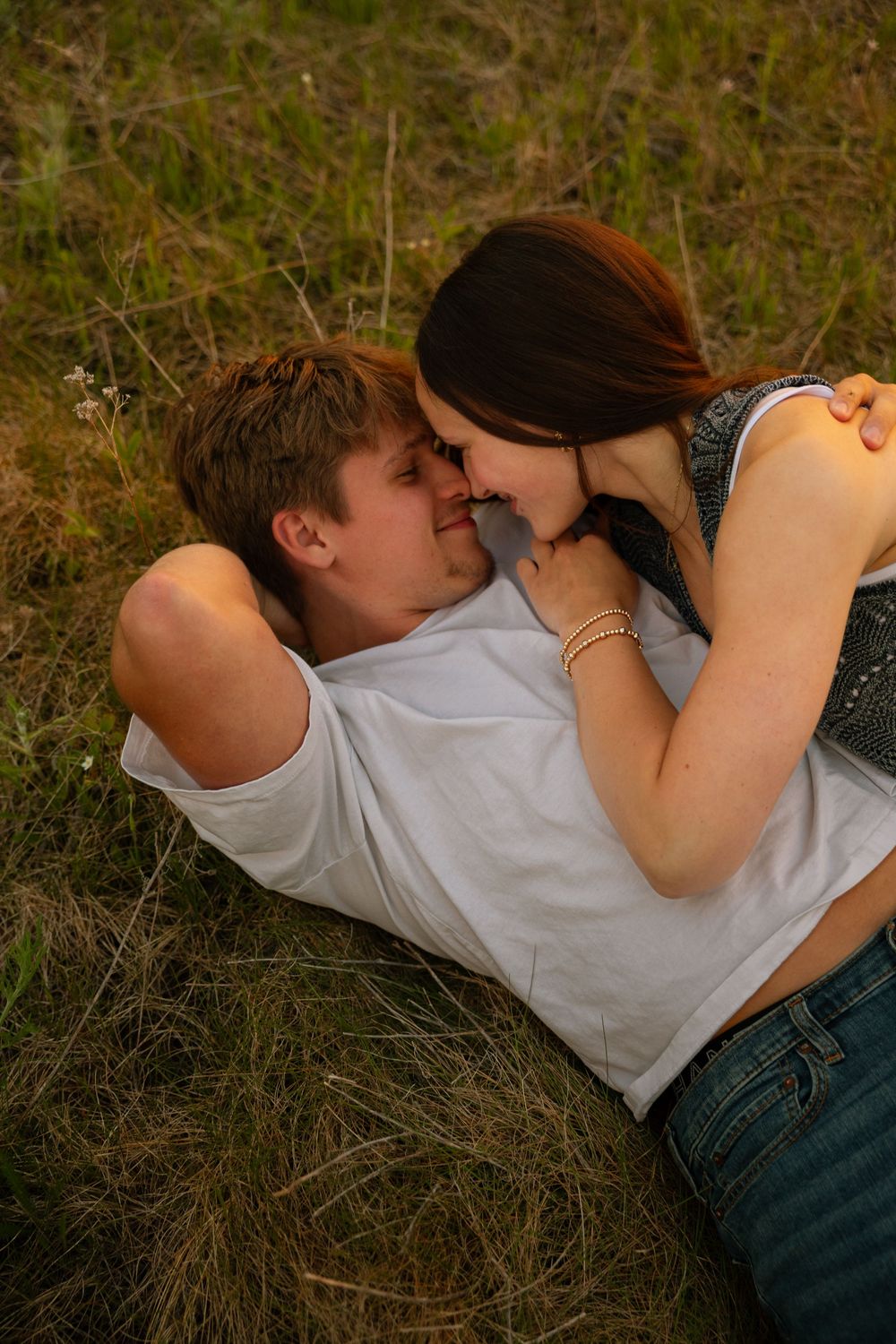 Young couple sharing a romantic moment lying in green grass field, noses touching and smiling at each other.