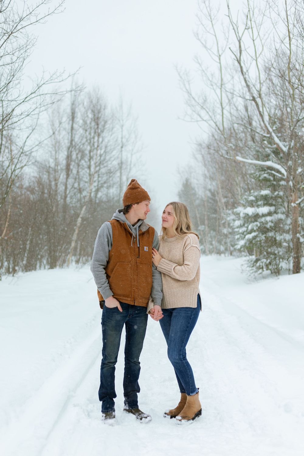 A couple shares a romantic moment while standing in a snowy winter landscape surrounded by bare trees.