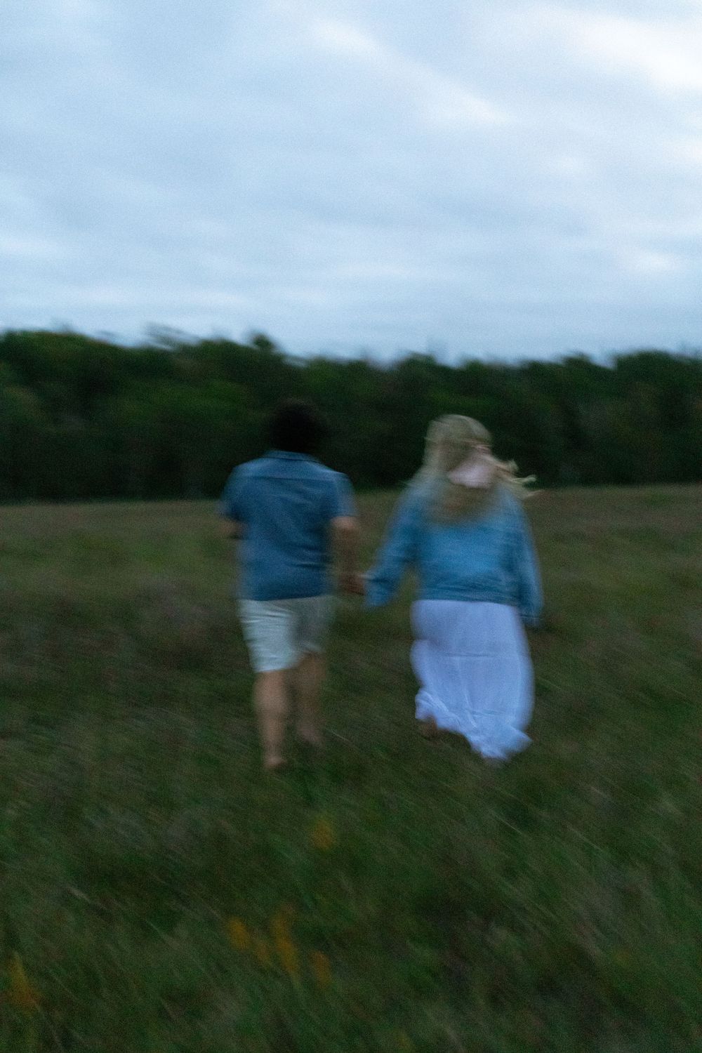 A group of people walk through a misty field at dusk wearing casual clothing.