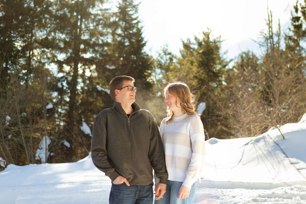 A couple shares a romantic moment in a snowy winter landscape surrounded by evergreen trees.