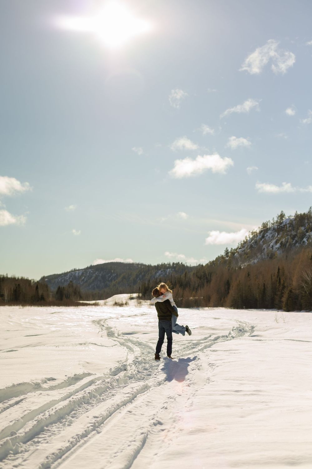 People skiing across a vast snow-covered landscape under bright blue winter skies with mountains in the distance.