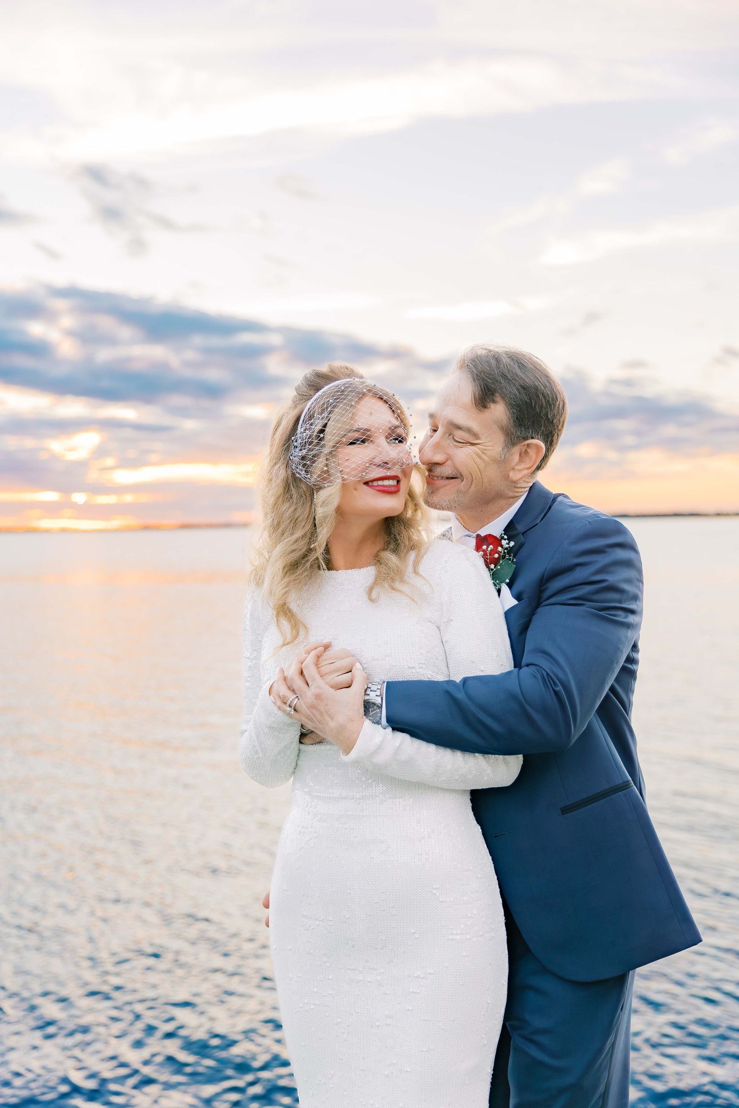 A romantic beach wedding portrait at sunset with water and colorful sky in the background.