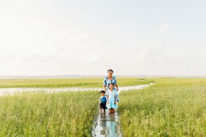 a mother and her two daughters strolling through the tall grass of the marsh