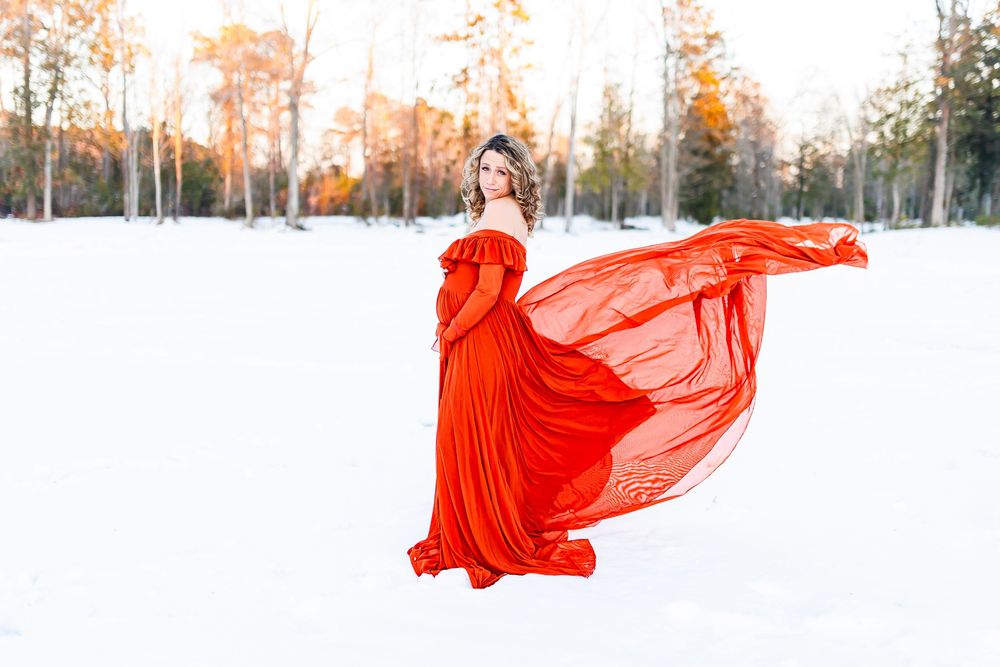 A figure in a flowing red dress dances gracefully across a snowy winter landscape at sunset.