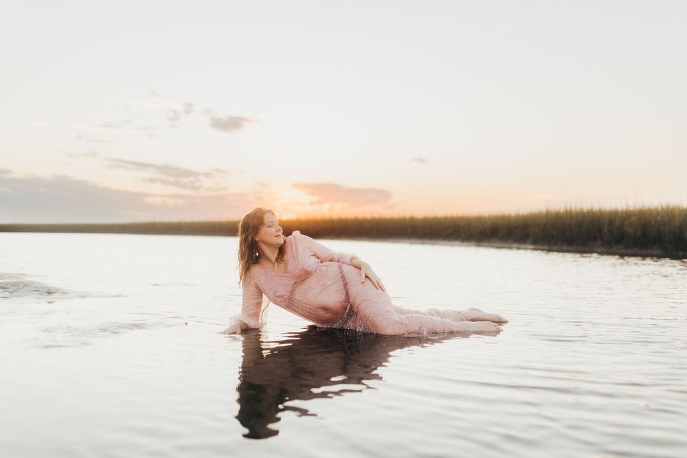 A person floats serenely in calm water during sunset, creating a peaceful and ethereal scene.