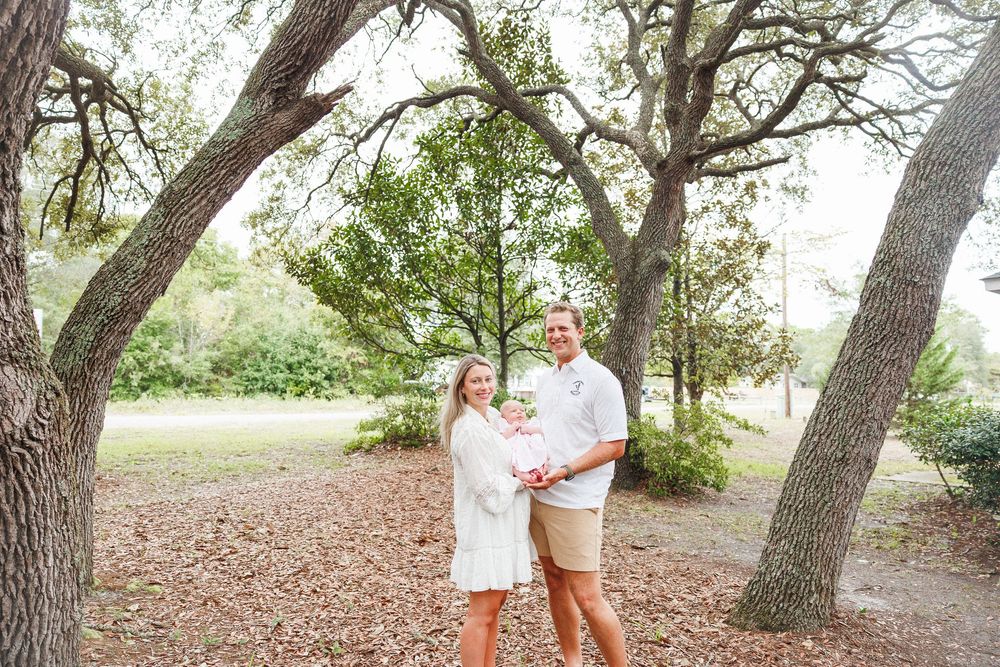 Couple smiling together outdoors under oak trees on a leaf-covered ground in a park setting.