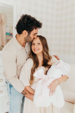 A romantic couple embraces in a bright room while wearing light colored clothing and jeans.