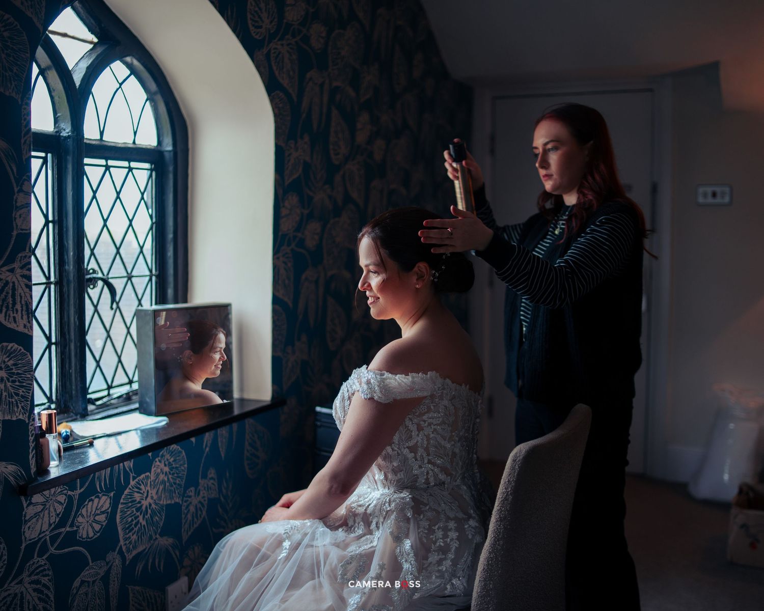 Wedding preparation scene with white lace dress near a gothic arched window with diamond panes in moody lighting.