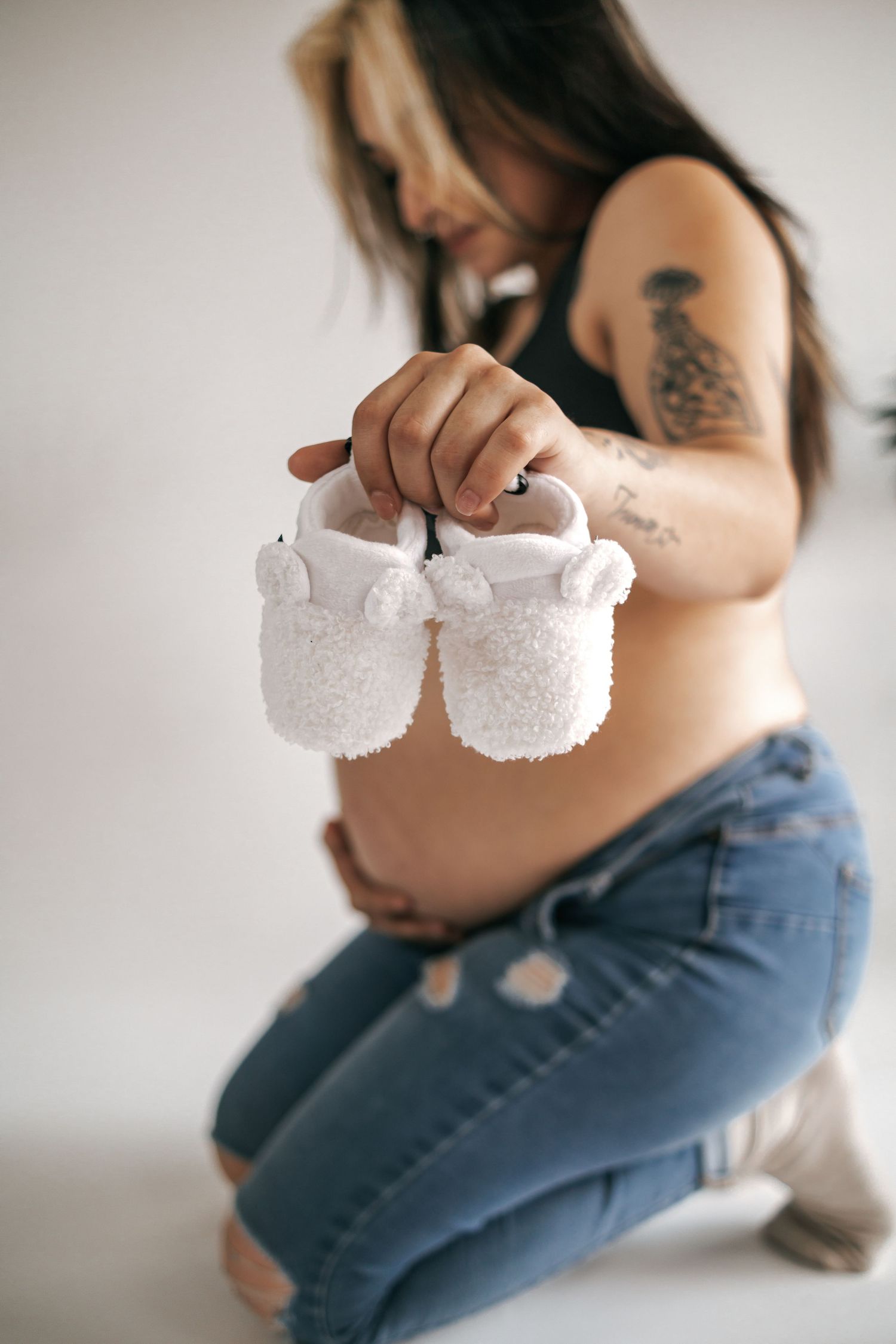 Maternity photography with expectant mother holding tiny white baby shoes.