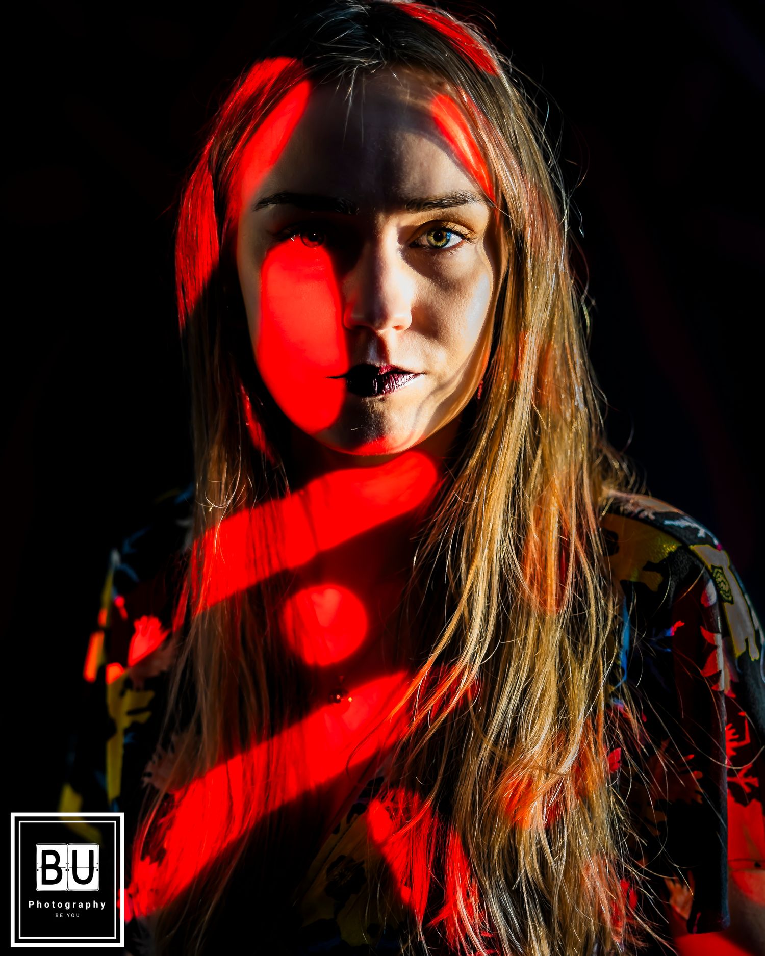 Creative portrait with dramatic red lighting and shadows across face.