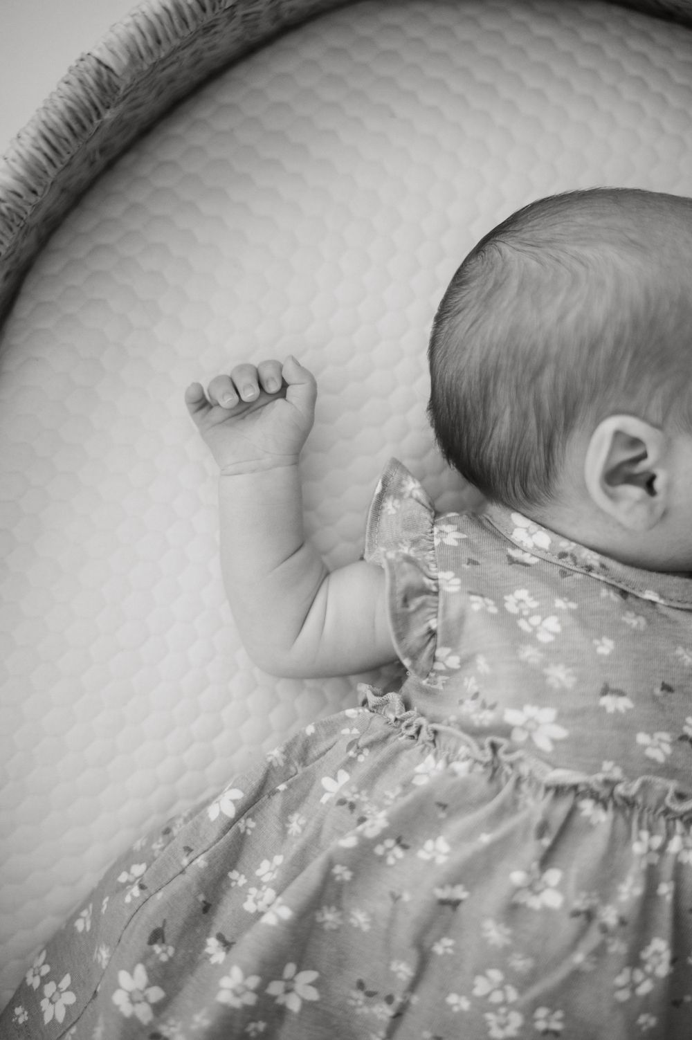 Top view of an infant's tiny hand grasping a floral patterned fabric on a white textured surface.