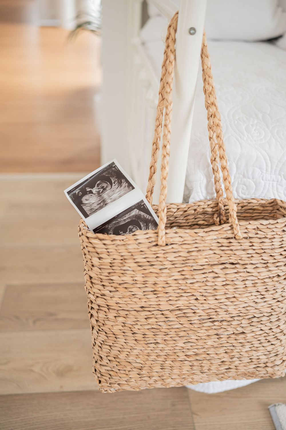 Woven straw basket with rope handles sits on light wooden floor with white photograph.