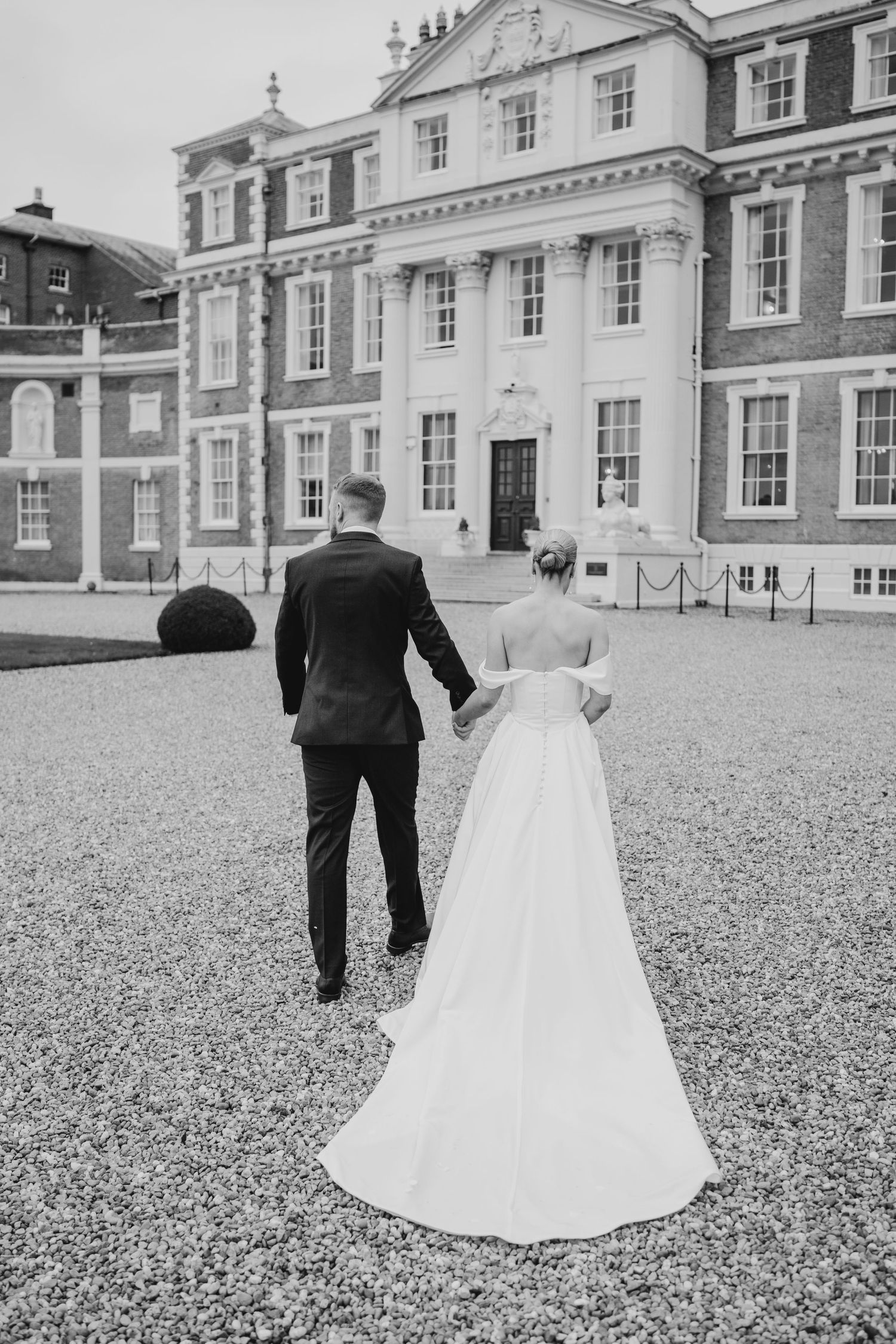 Classic black and white photo of newlyweds walking towards an elegant historic mansion.