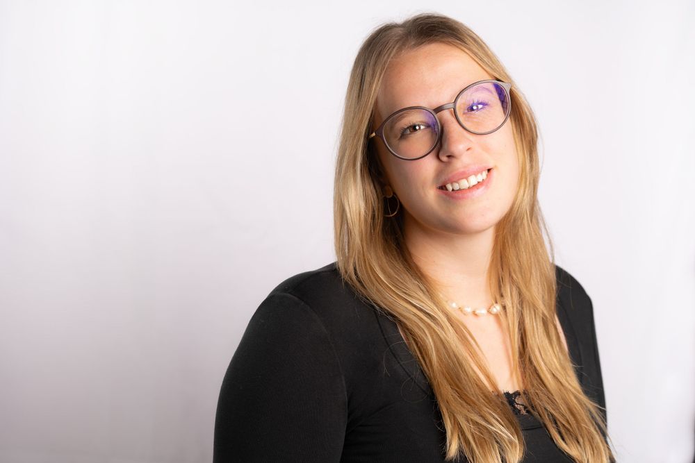Professional headshot of a person wearing glasses and black top against white background.