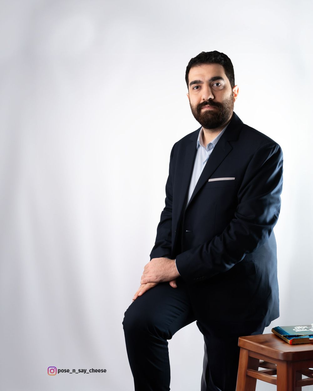 Professional studio portrait of a businessman in a navy suit seated against a light gray background.