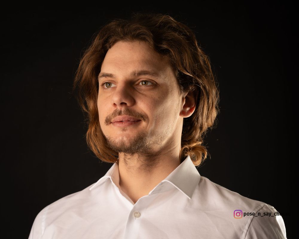 Studio portrait of a person in white shirt with long hair against dark background.