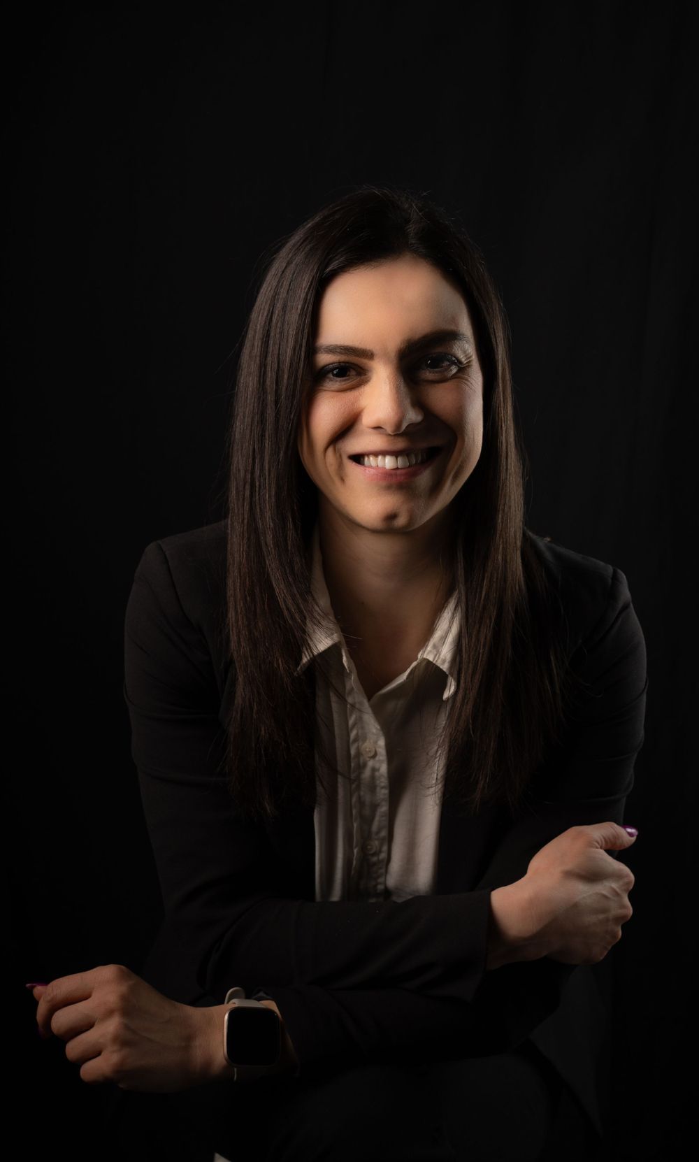 Professional headshot of a person in business attire smiling warmly against a dark background.