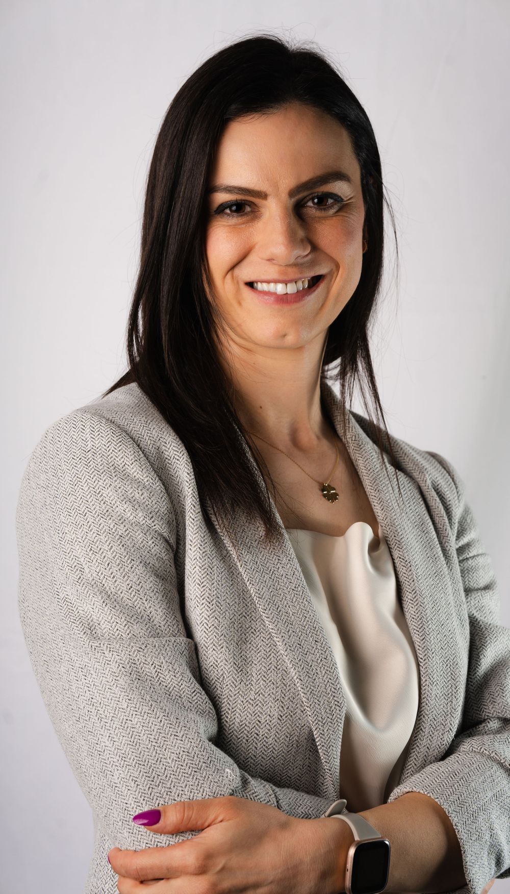 Professional headshot of a person in a gray blazer and white top against light background.