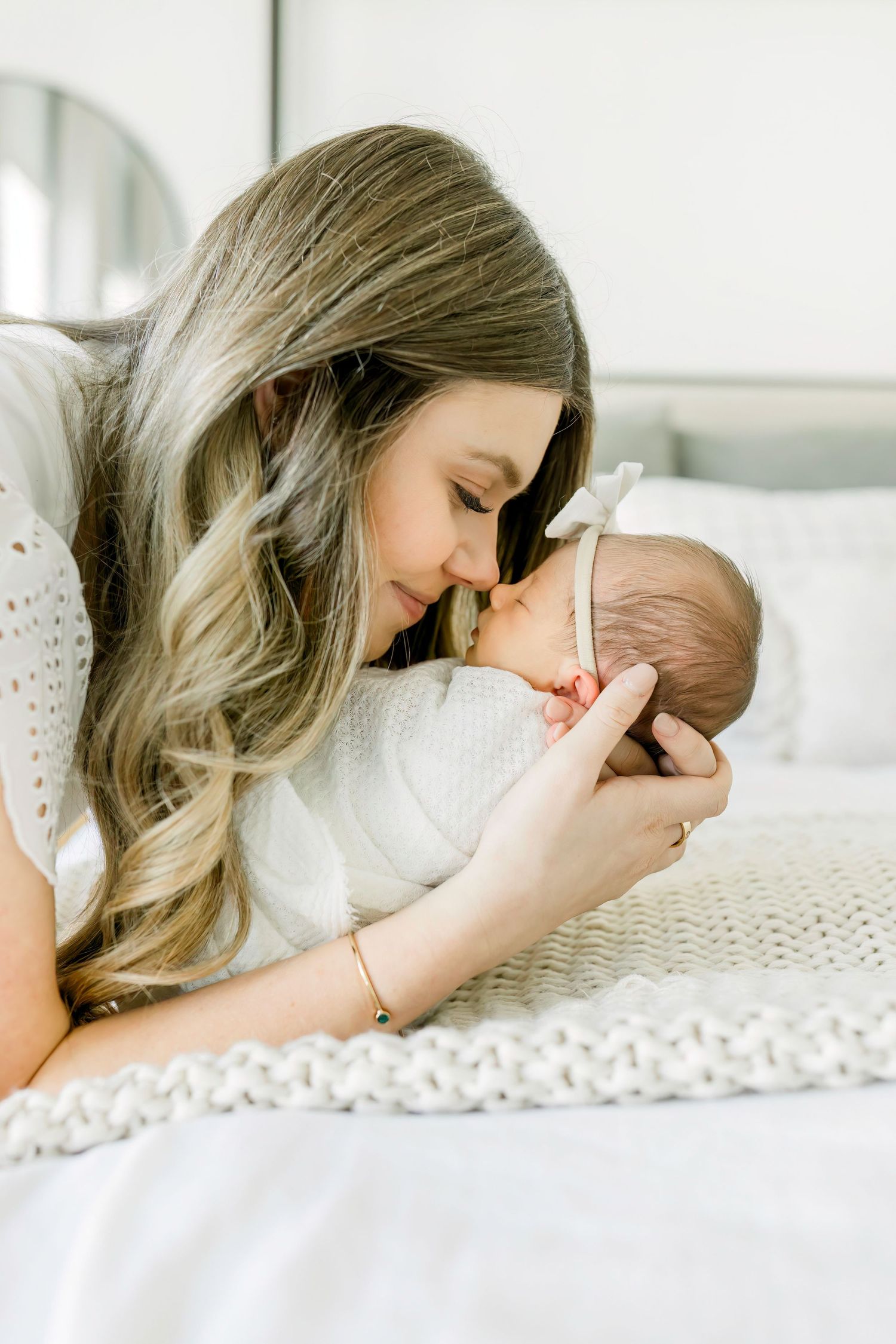 Tender moment between parent and sleeping newborn on white knitted blanket.
