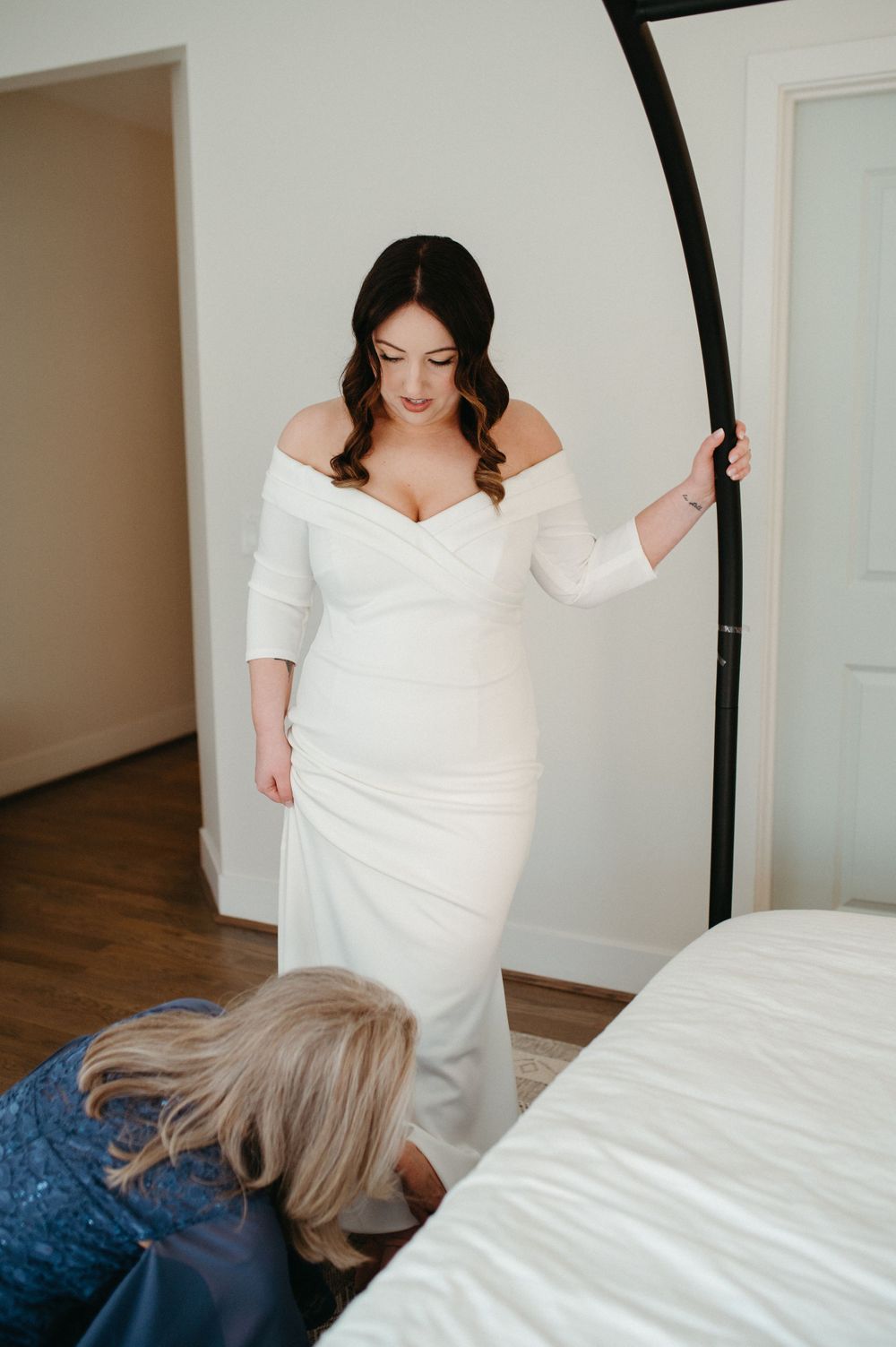 A bride in an off-shoulder wedding gown poses during a fitting session.