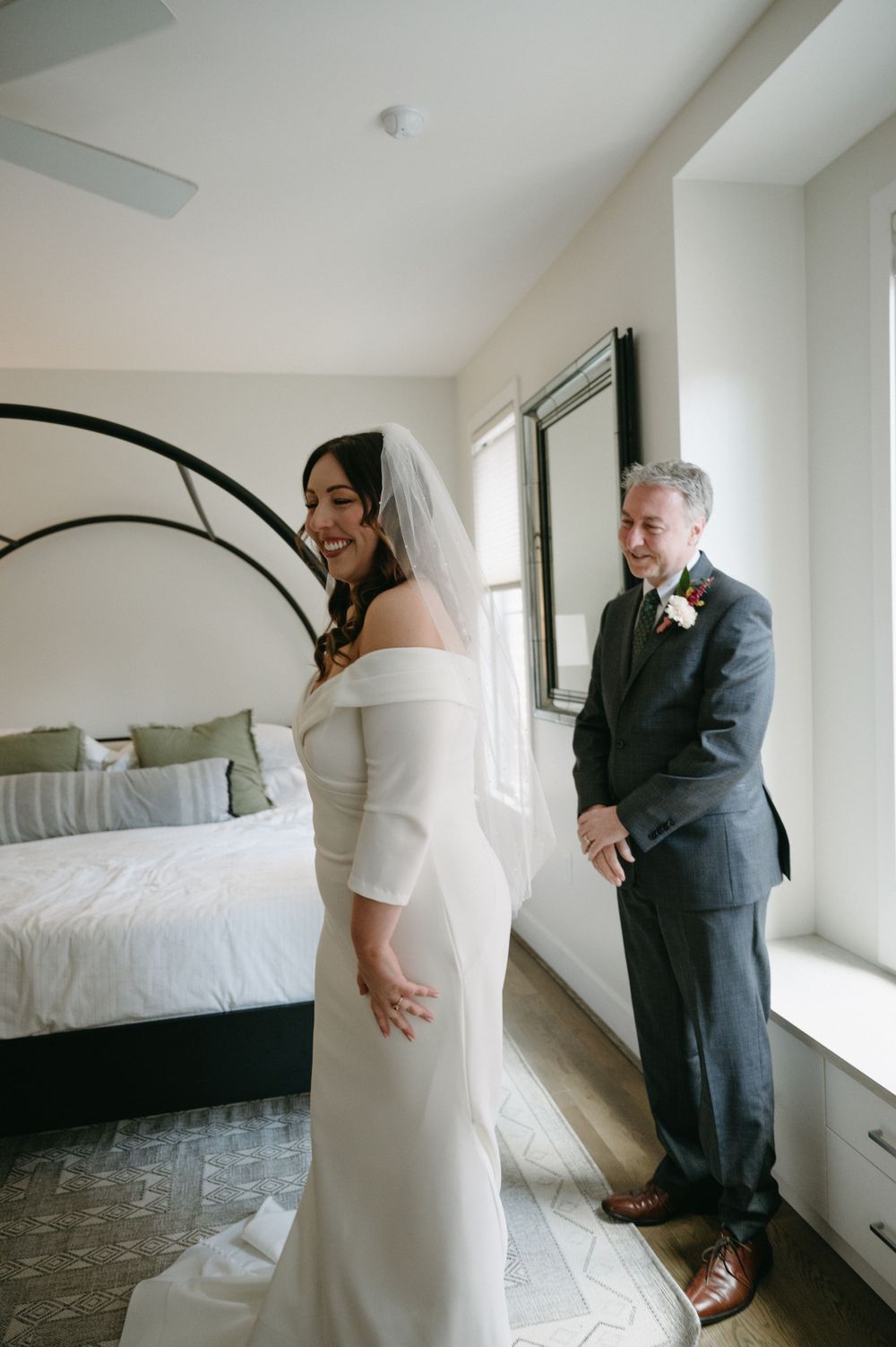 A candid wedding moment captured in a modern bedroom with black metal bed frame.