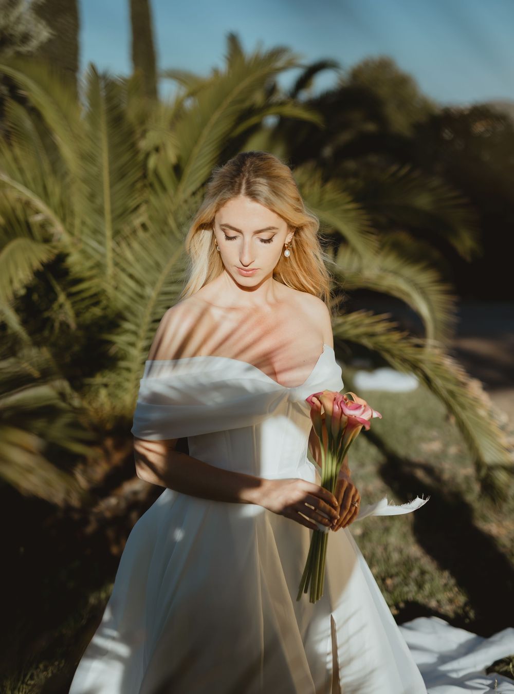 Ethereal bridal portrait in white dress against palm trees and sunlight.